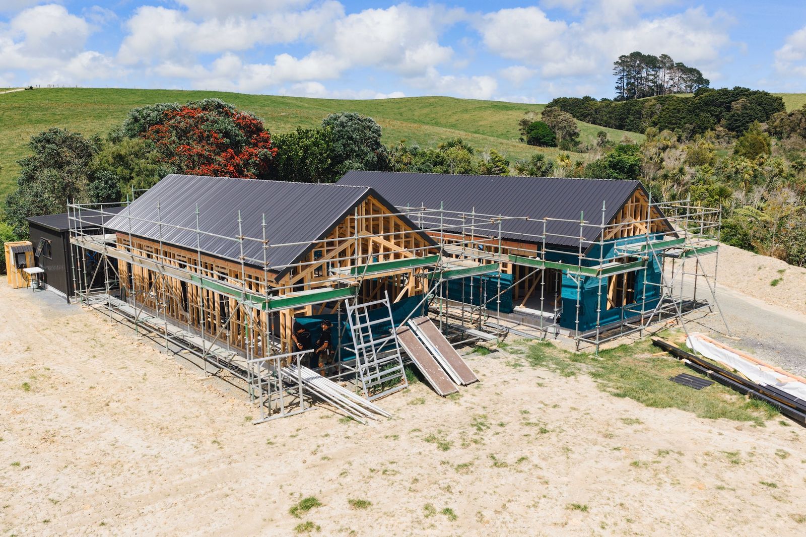 Large family home under construction in Mangawhai with multi-gable roof and native bush backdrop