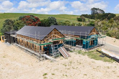 Large family home under construction in Mangawhai with multi-gable roof and native bush backdrop
