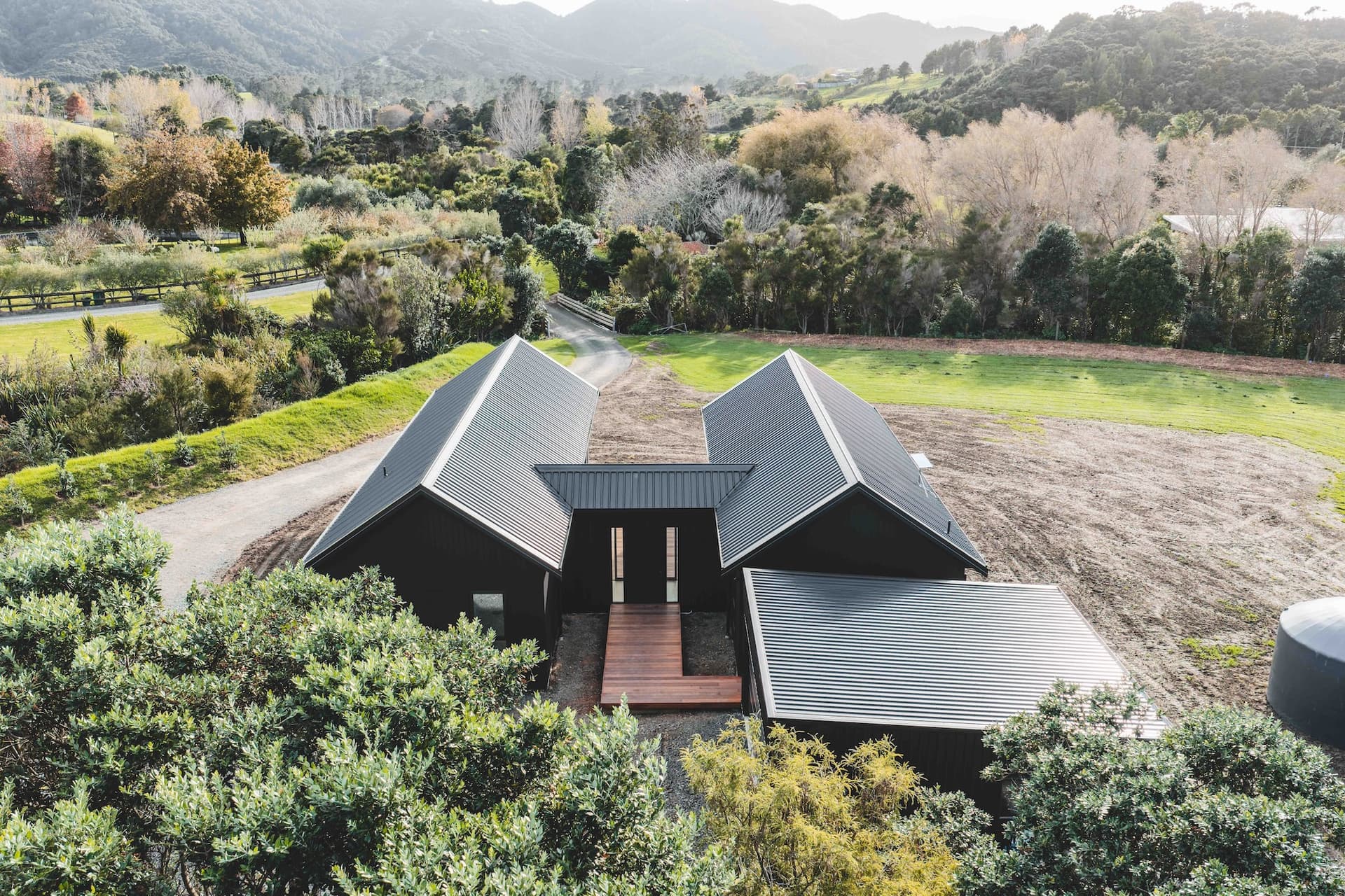 Aerial view of a twin-gable rural home built by Boaz Developments, set in native planting with Northland hills behind