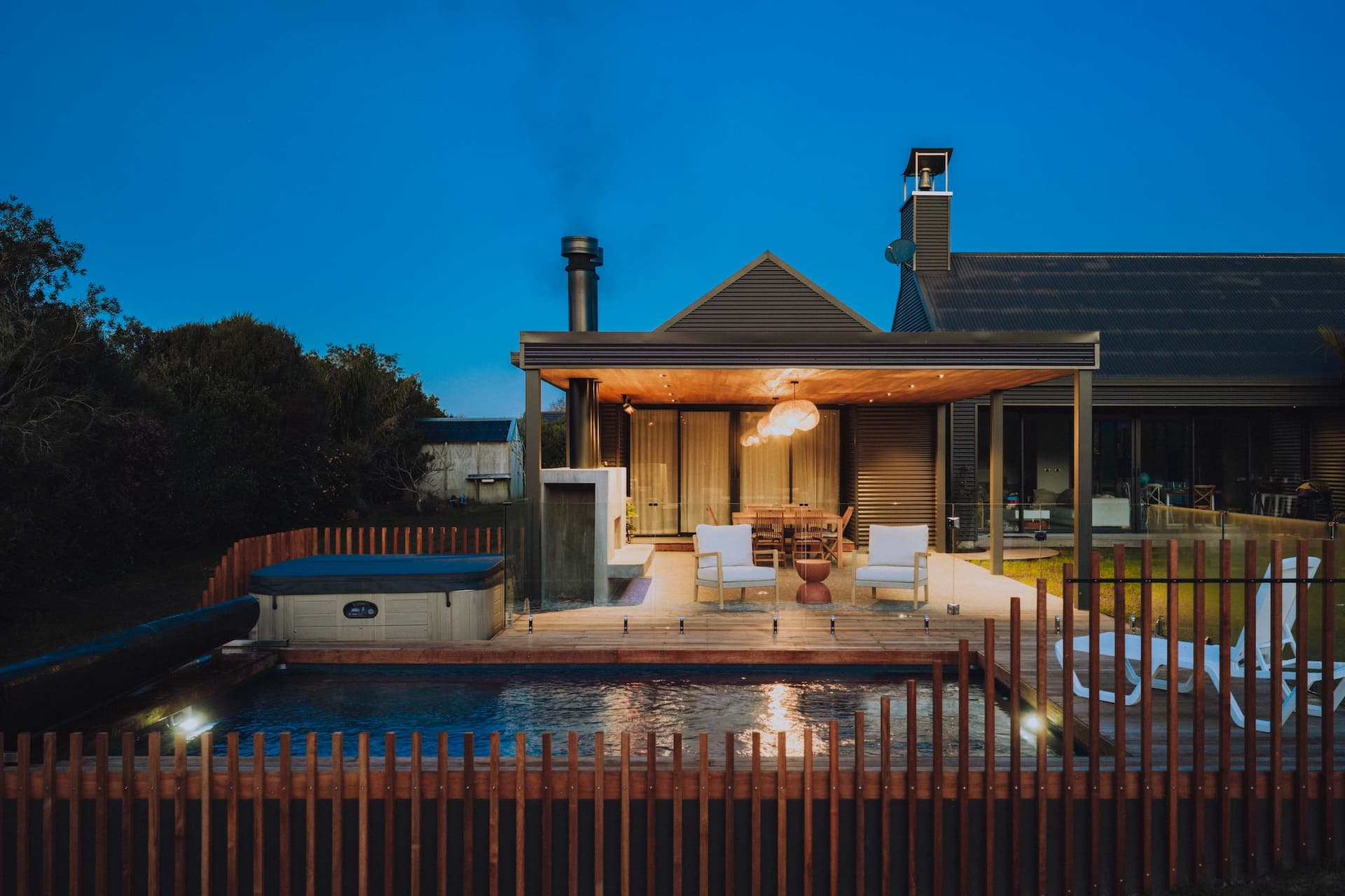 Finished outdoor living area at dusk in Mangawhai Heads with in-ground pool, covered entertaining pavilion and spa